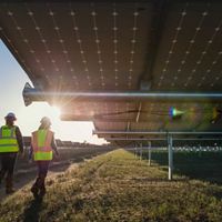 Two workers walk along rows of solar panels.
