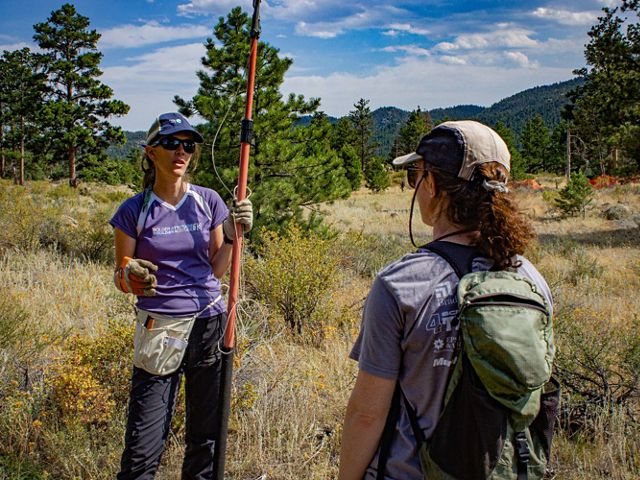 Catherine Schloegel holds a tree pruner while talking to a local researcher about seed cone collection in 2019.
