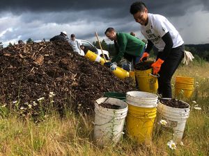 Smiling volunteers with buckets bending over a pile of dirt.