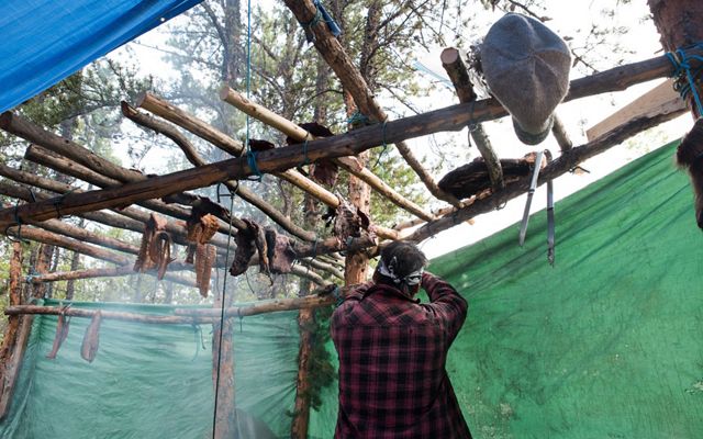 first nation man smokes and dries caribou outside on wooden poles in the northwest territories