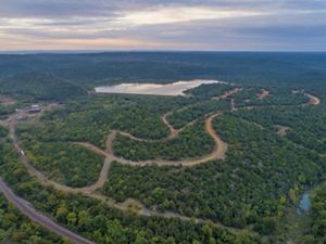 Aerial view of an expanse of green forest and twisting dirt roads with a lake in the middle.