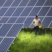 Photo of a man holding a hardhat standing to the right of a large array of newly installed solar panels.