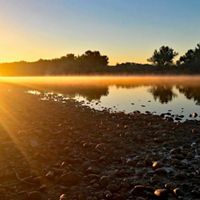 Photo of a sunrise over a river, with rocks in the foreground.
