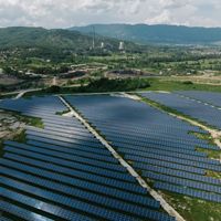 Aerial view of a field of solar panels in a wide, green landscape.