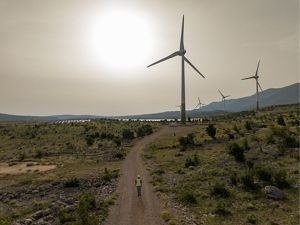 Aerial of several large wind turbines across a hilly landscape.