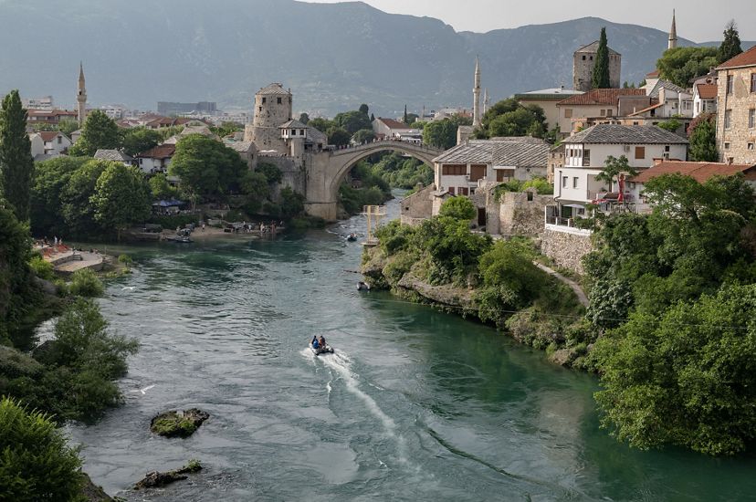 A large arched stone bridge and various old stone buildings surround the Nerevta River.