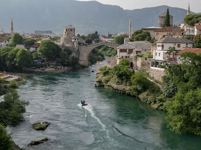 A large arched stone bridge and various old stone buildings surround the Nerevta River.