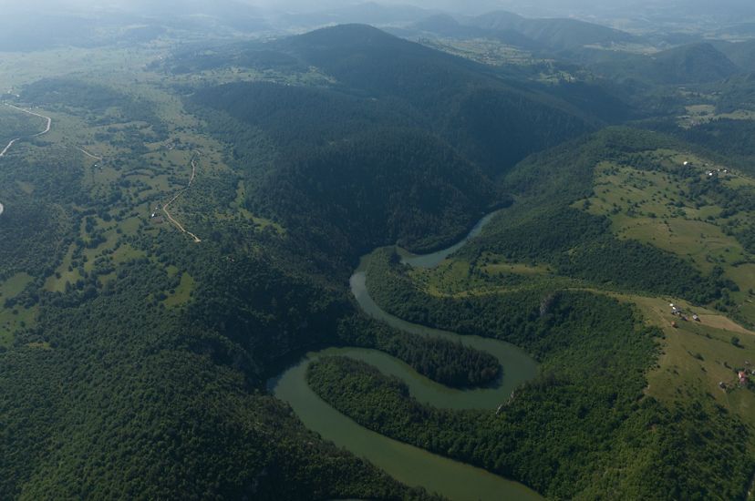 Aerial of a river full of oxbow curves brushing up against hilly terrain and farmland.