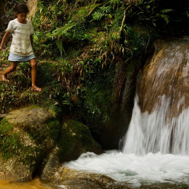 A young girl walks along the rocky edge next to a short waterfall.